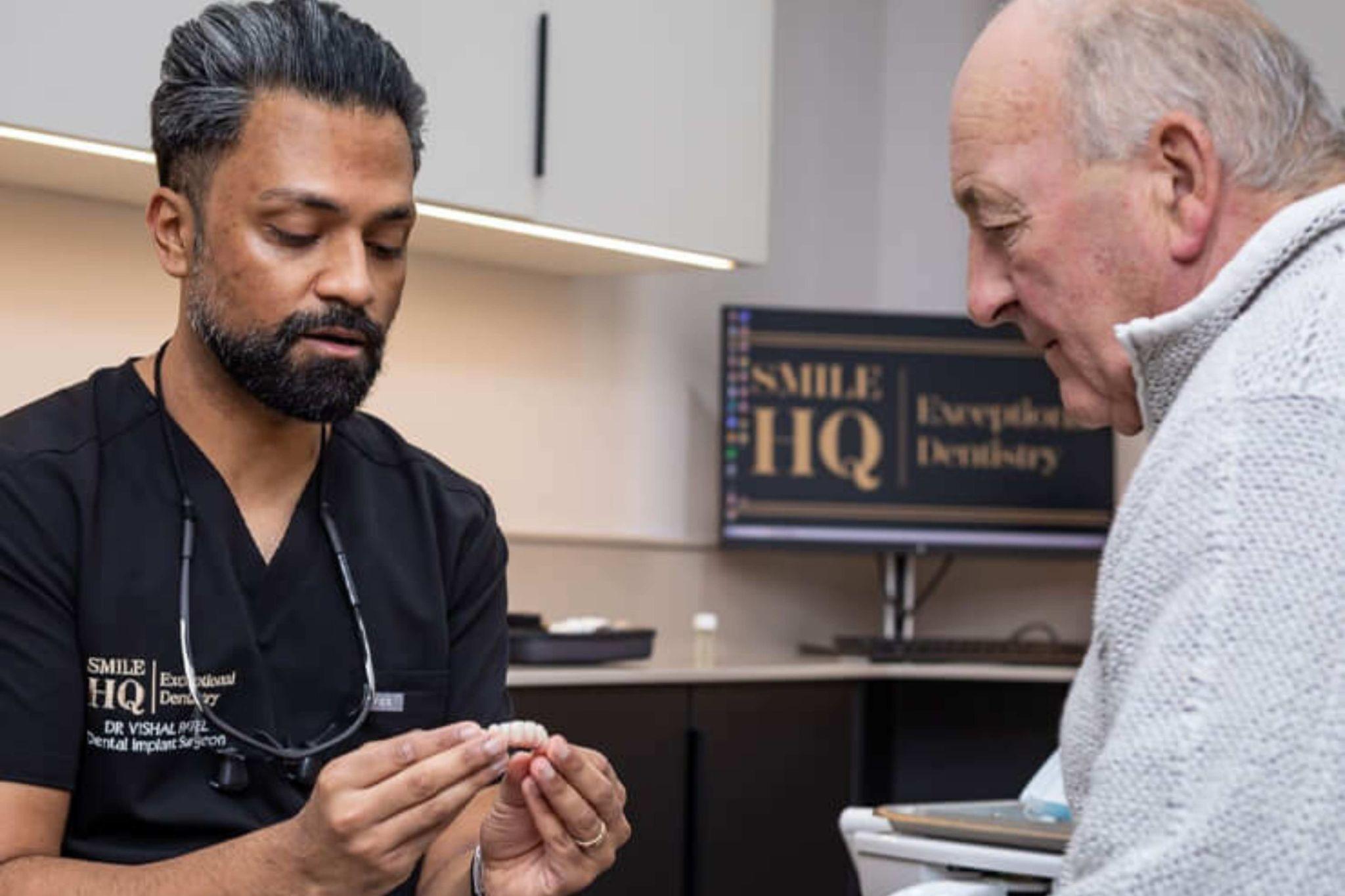 Dr Vishal Patel explaining dental implant procedure using model to patient in Essex dental clinic SmileHQ Brentwood