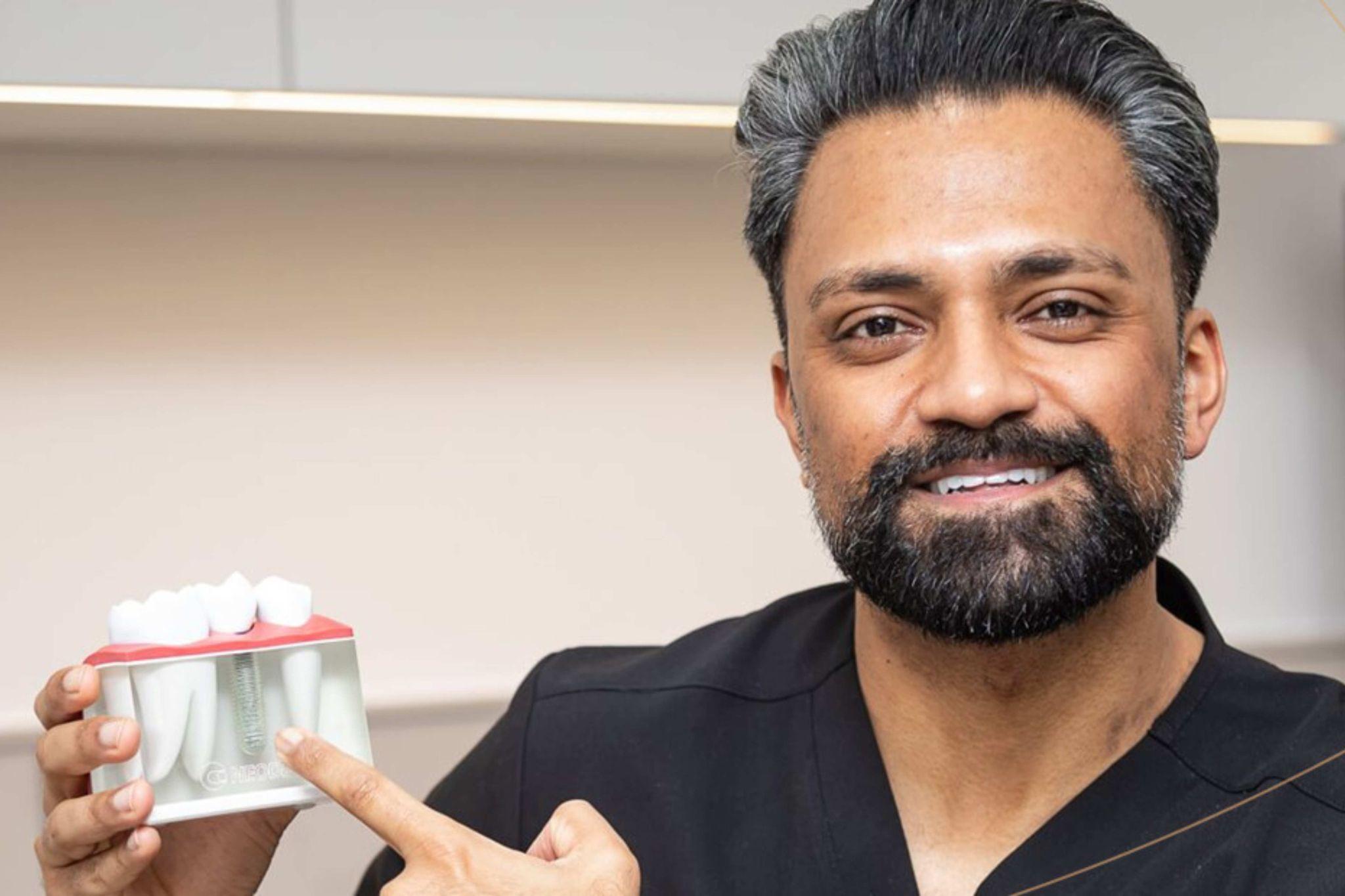 Dr Vishal Patel holding dental implant model explaining suitability for dental implants Essex SmileHQ Brentwood