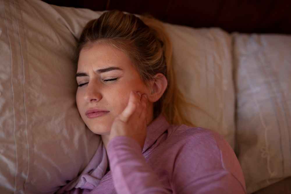 Woman experiencing jaw pain from teeth grinding at night